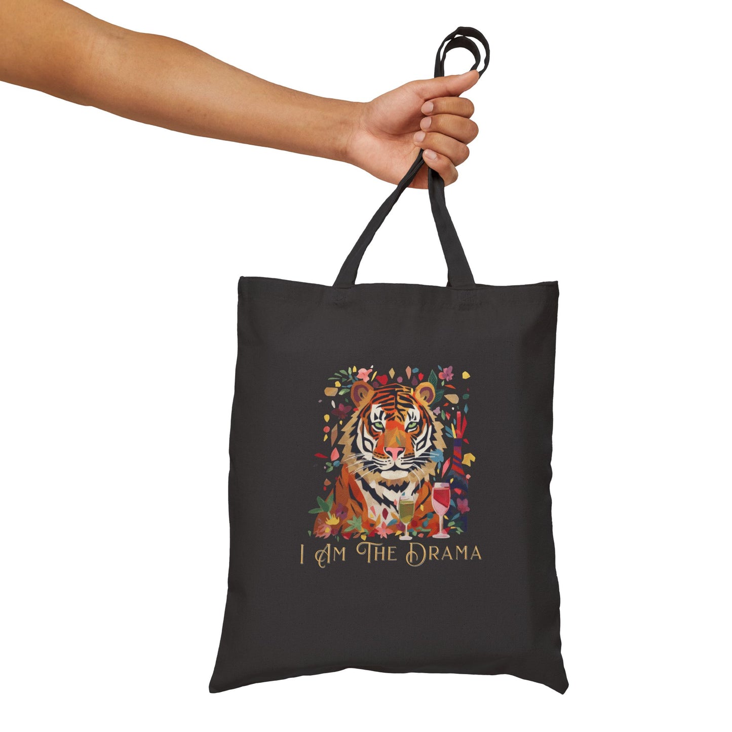 Black tote bag with a tiger design and 'I AM THE DRAMA' text, held by a hand against a white background.