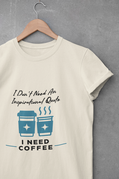 Beige t-shirt with 'I Don't Need An Inspirational Quote, I Need Coffee' text and graphic on a hanger against a gray background.