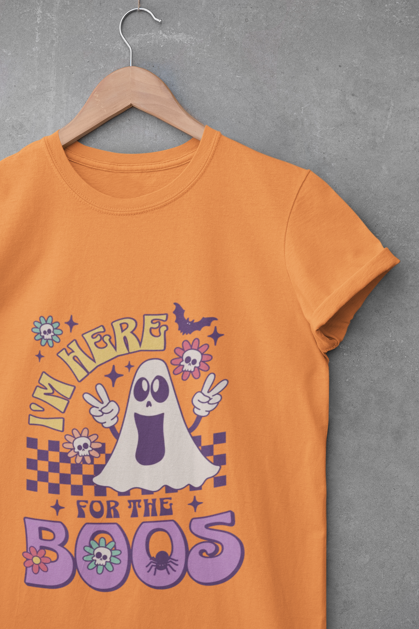 Orange t-shirt with a ghost graphic and text on a hanger against a gray background