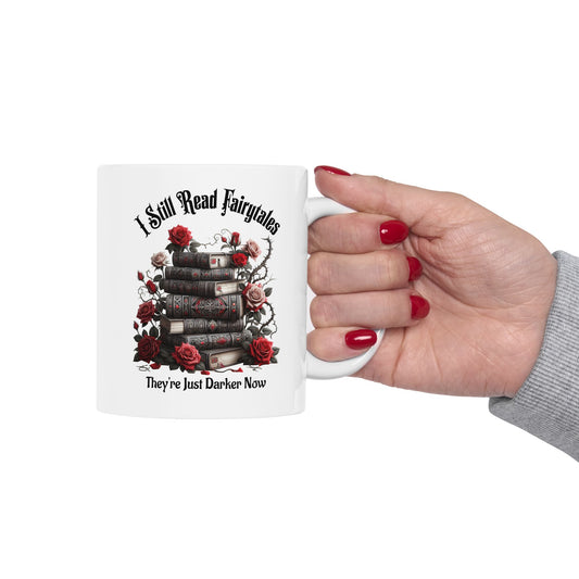 Mug with book and rose design held by a hand with red nail polish on a white background