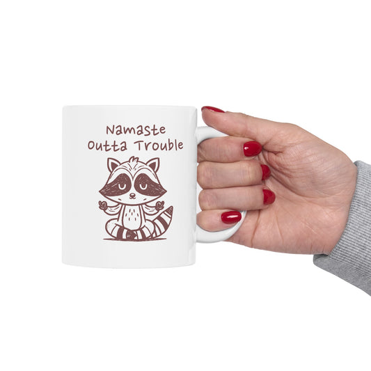 White mug with a raccoon design and text, held by a hand with red nail polish.